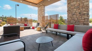 An outdoor patio area with stone pillars, a wooden ceiling, and a seating arrangement including sofas and chairs.