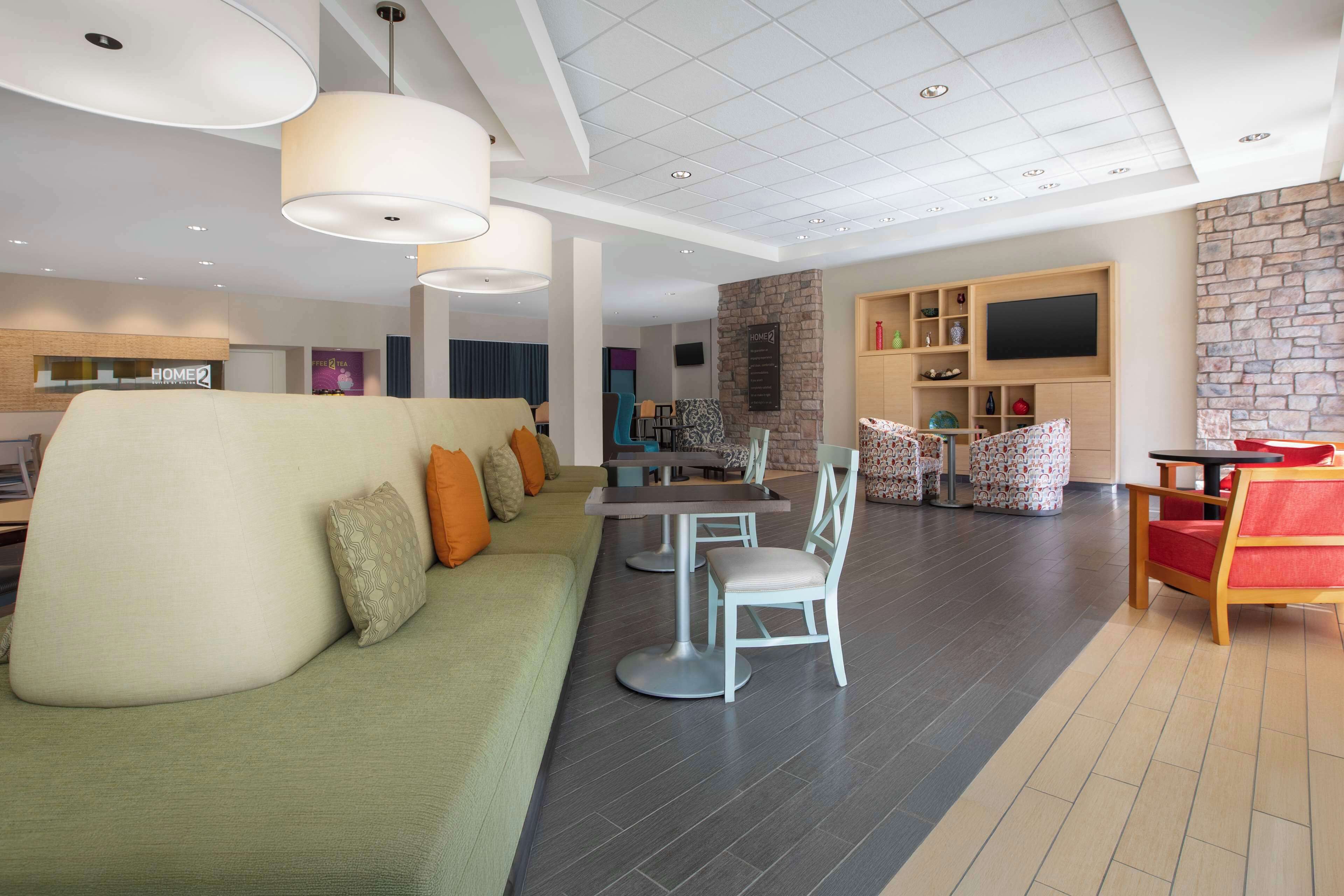 A modern living room with a green sofa, white chairs, a dining table, and a TV mounted on a stone wall.