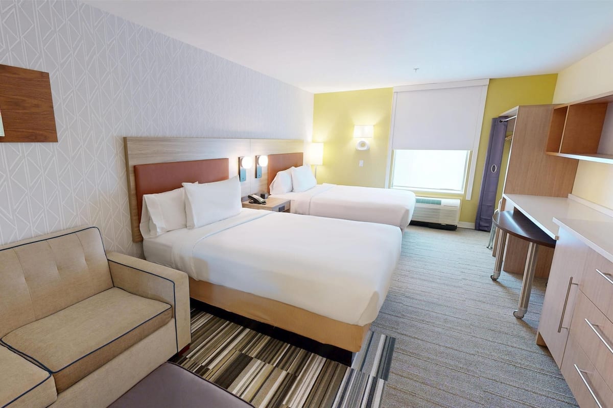 A hotel room with two beds, a sofa, a desk, and a painting on the wall.