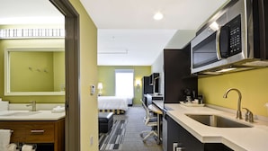 A hotel room with a kitchenette, a large mirror, a bed, and a bathroom with a sink and toilet.