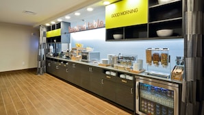 A modern breakfast bar with a 'Good Morning' sign, a 'Inspired Table' sign, and a refrigerated display with beverages.