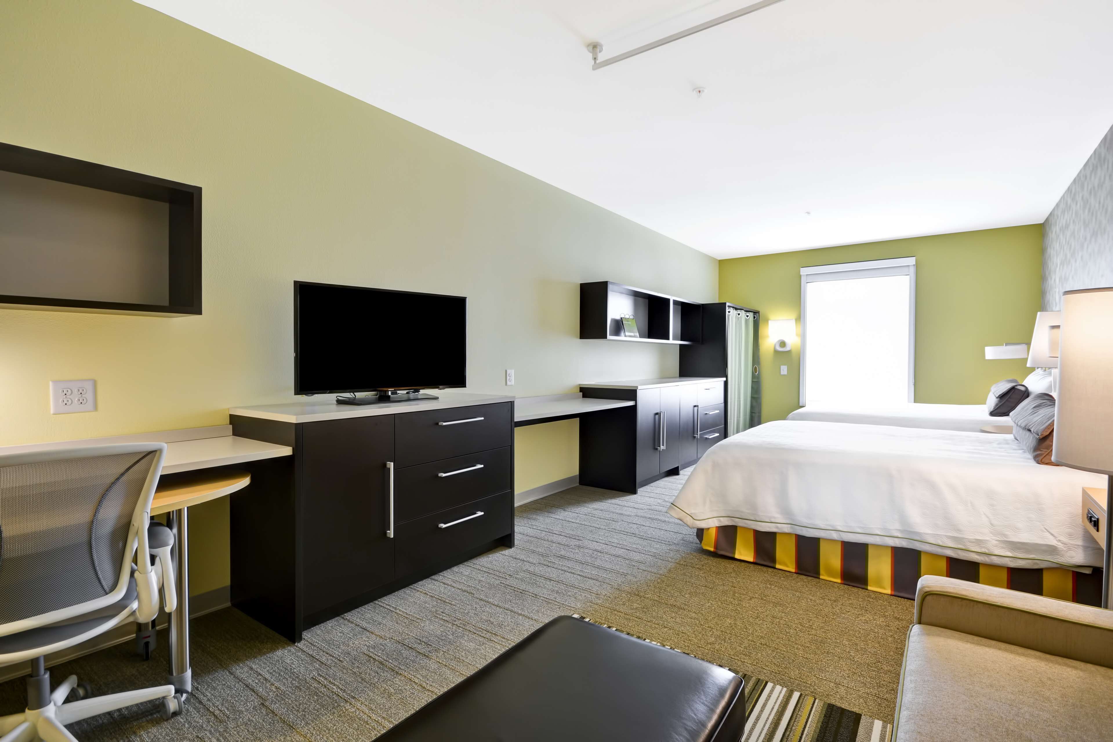 Una habitación de hotel con cama, escritorio, silla, televisión y ventana.