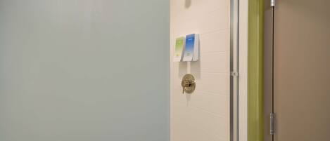 Un baño con mampara de vidrio, un perchero y un panel de control en la pared.