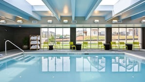 An indoor swimming pool with clear glass ceilings, a view of the outside, and yellow chairs and a towel rack.