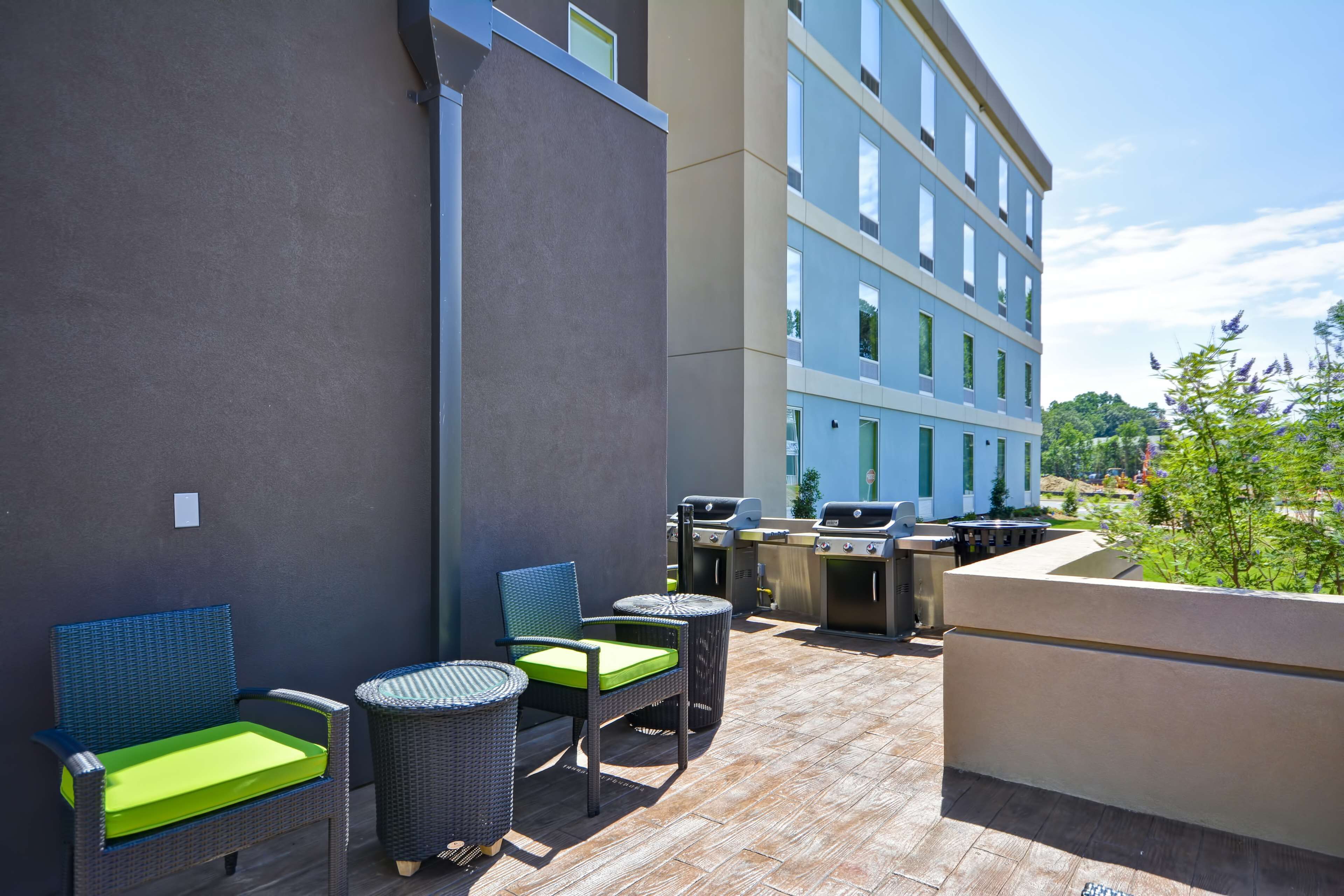 Eine Terrasse im Freien mit Korbmöbeln, einem Grill und einem Gebäude im Hintergrund.