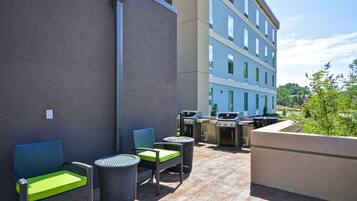 Eine Terrasse im Freien mit Korbmöbeln, einem Grill und einem Gebäude im Hintergrund.