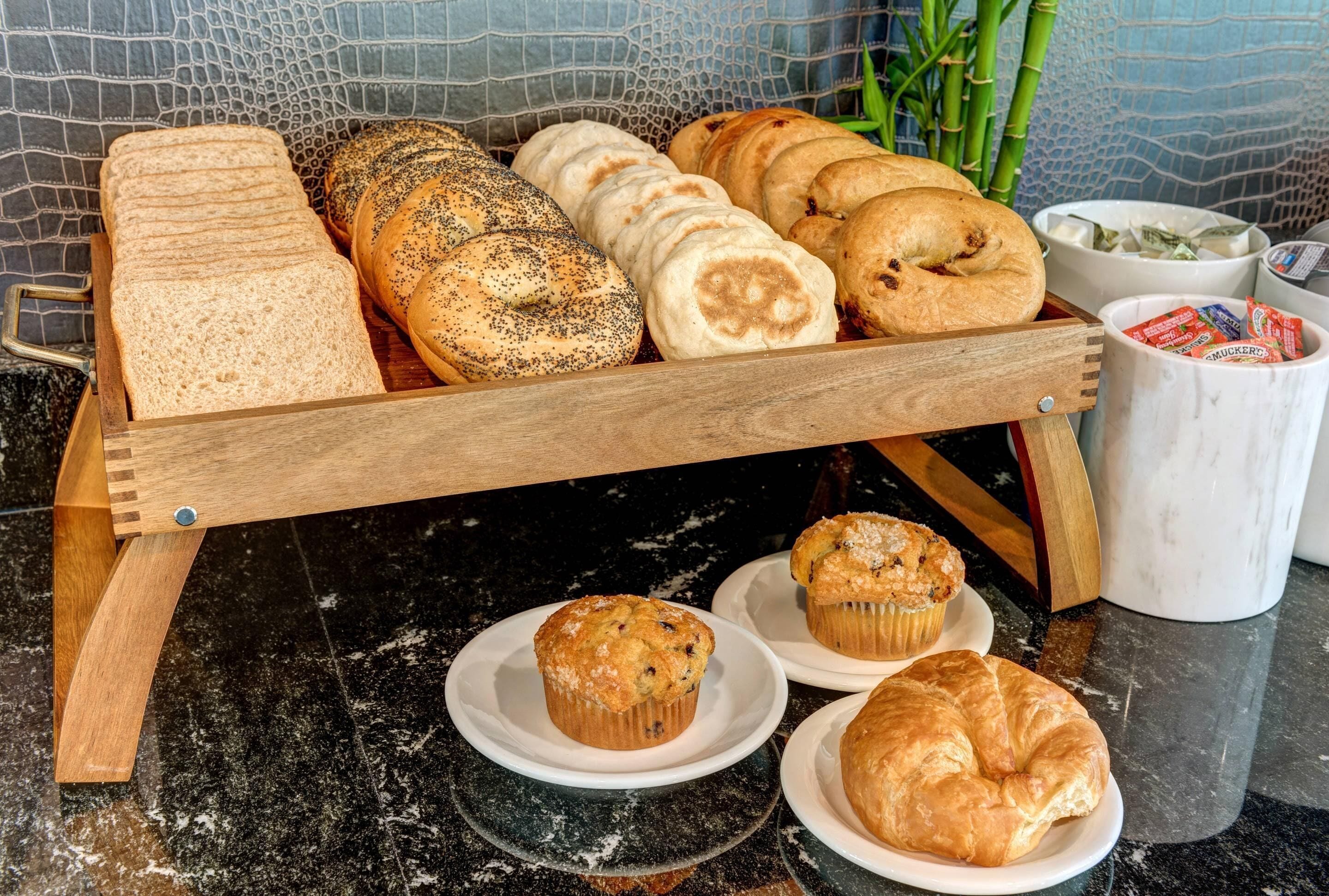 A wooden bread display with various types of bread and pastries, including muffins and croissants, on a marble countertop.