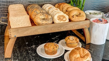 A wooden bread display with various types of bread and pastries, including muffins and croissants, on a marble countertop.