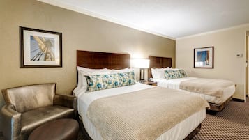 A hotel room with two beds, a chair, a lamp, and framed pictures on the walls.