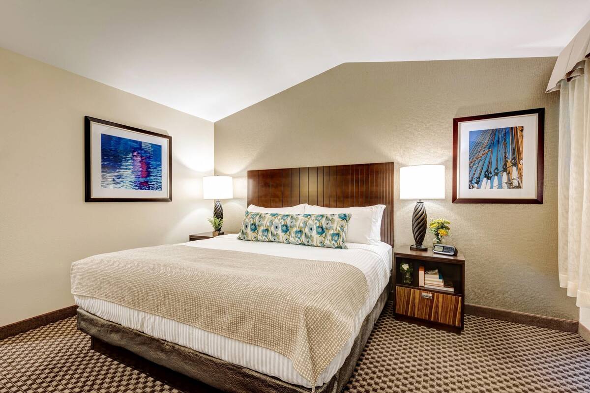 Une chambre d’hôtel avec un grand lit, deux tables de chevet, une tête de lit et deux tableaux encadrés accrochés aux murs.