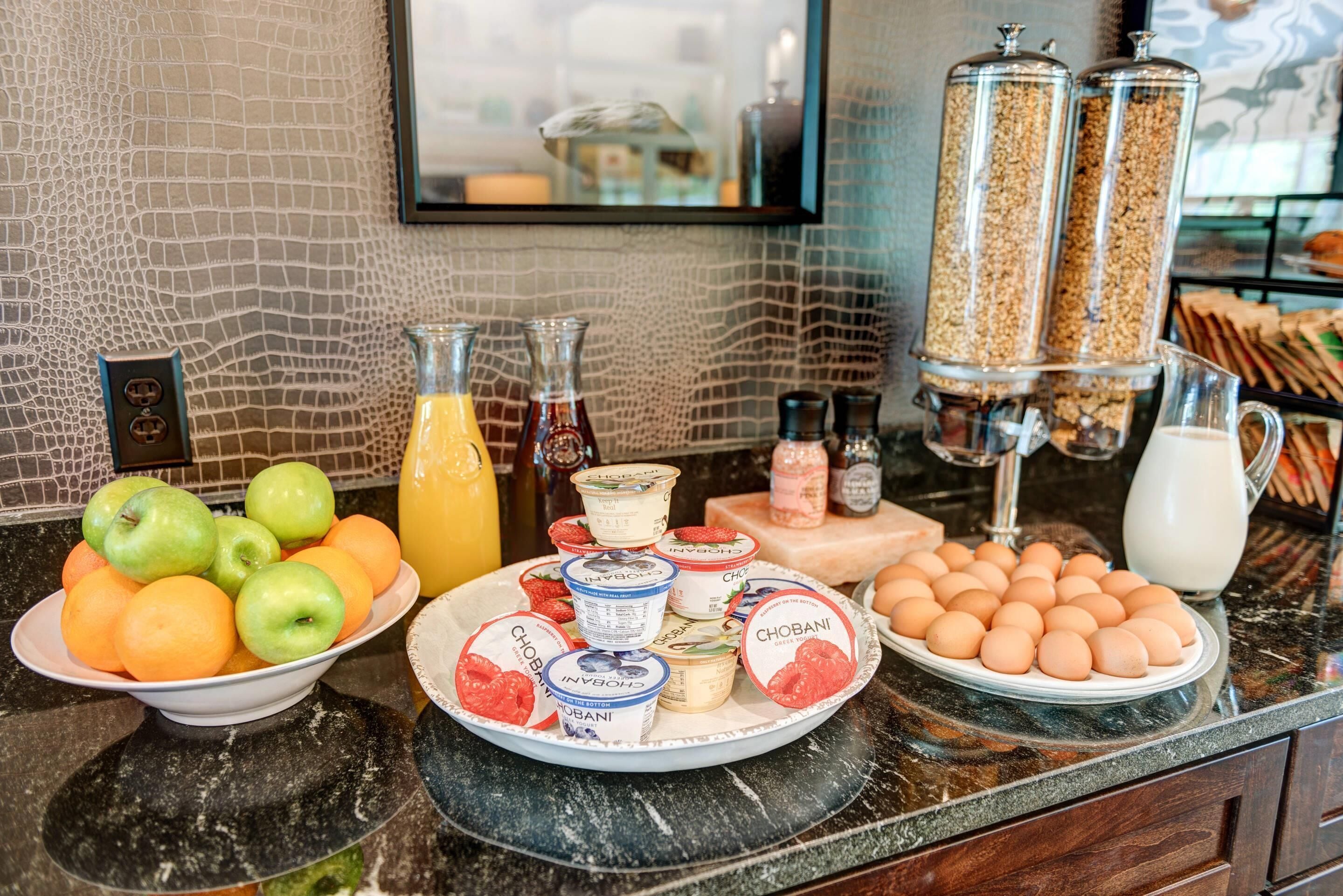 A breakfast buffet with fruits, yogurt, eggs, and cereal.
