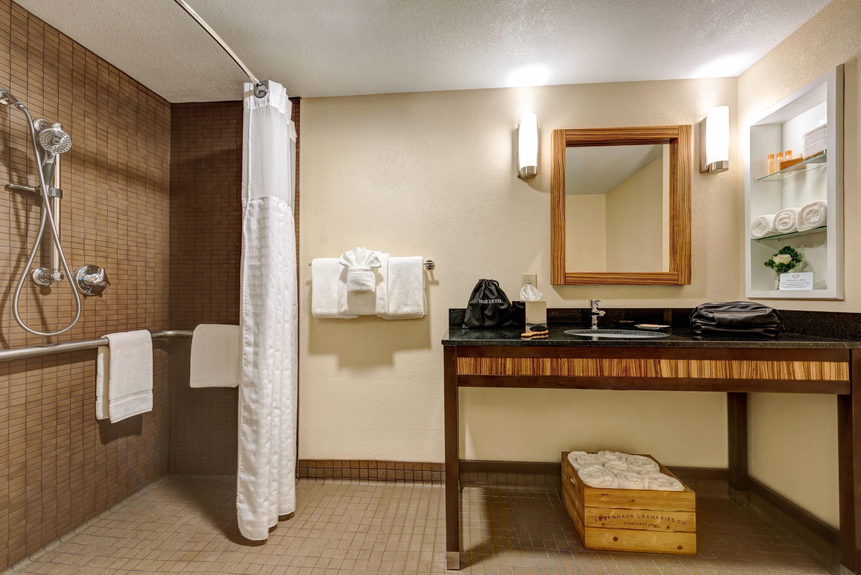 Un baño con ducha, lavabo, espejo y toallero.