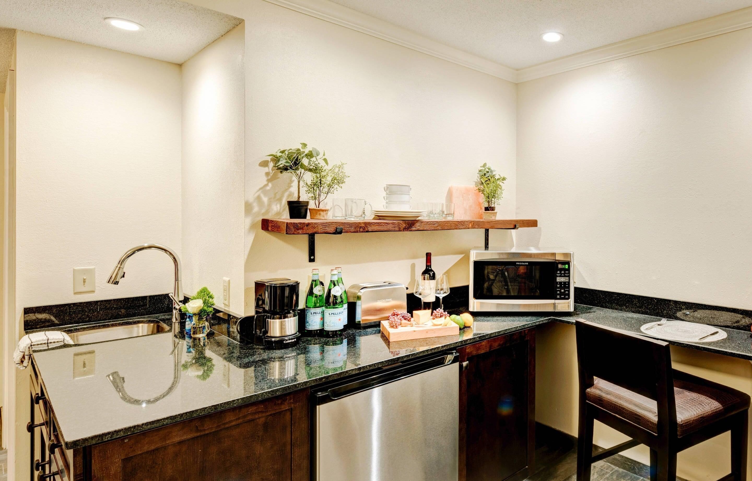 A kitchen with a stainless steel sink, a microwave, a toaster, and a wooden shelf with plants.