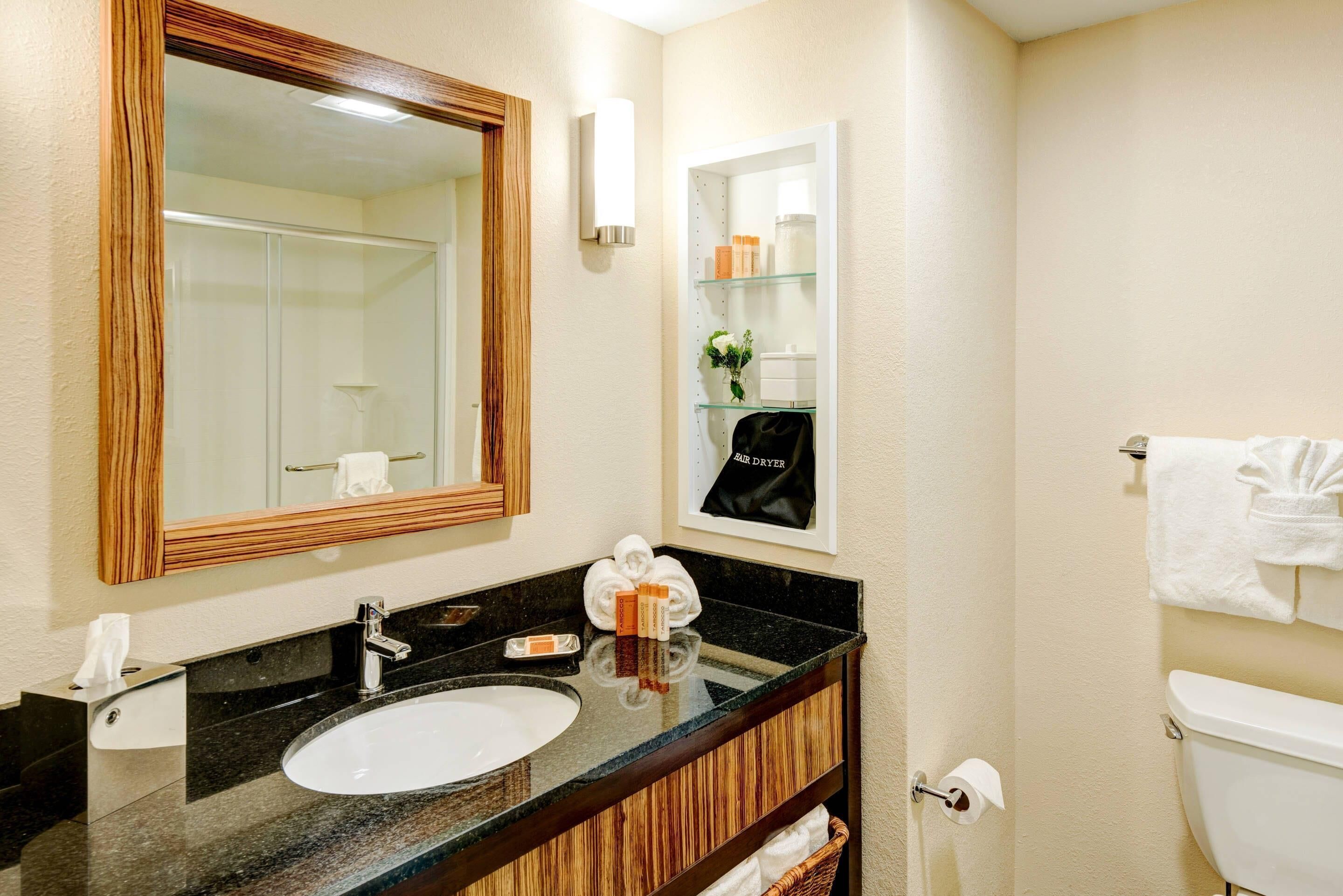 A bathroom with a wooden vanity, a large mirror, a sink, a towel rack, and a toilet.