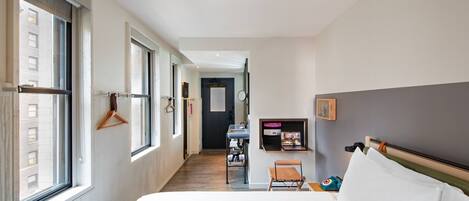 Habitación de hotel con una cama grande, un escritorio y una silla. Hay una ventana al lado izquierdo y una puerta al final de la habitación.