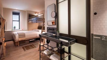 Una habitación de hotel moderna con literas, un escritorio pequeño con espejo, un lavabo y una ventana con vistas.