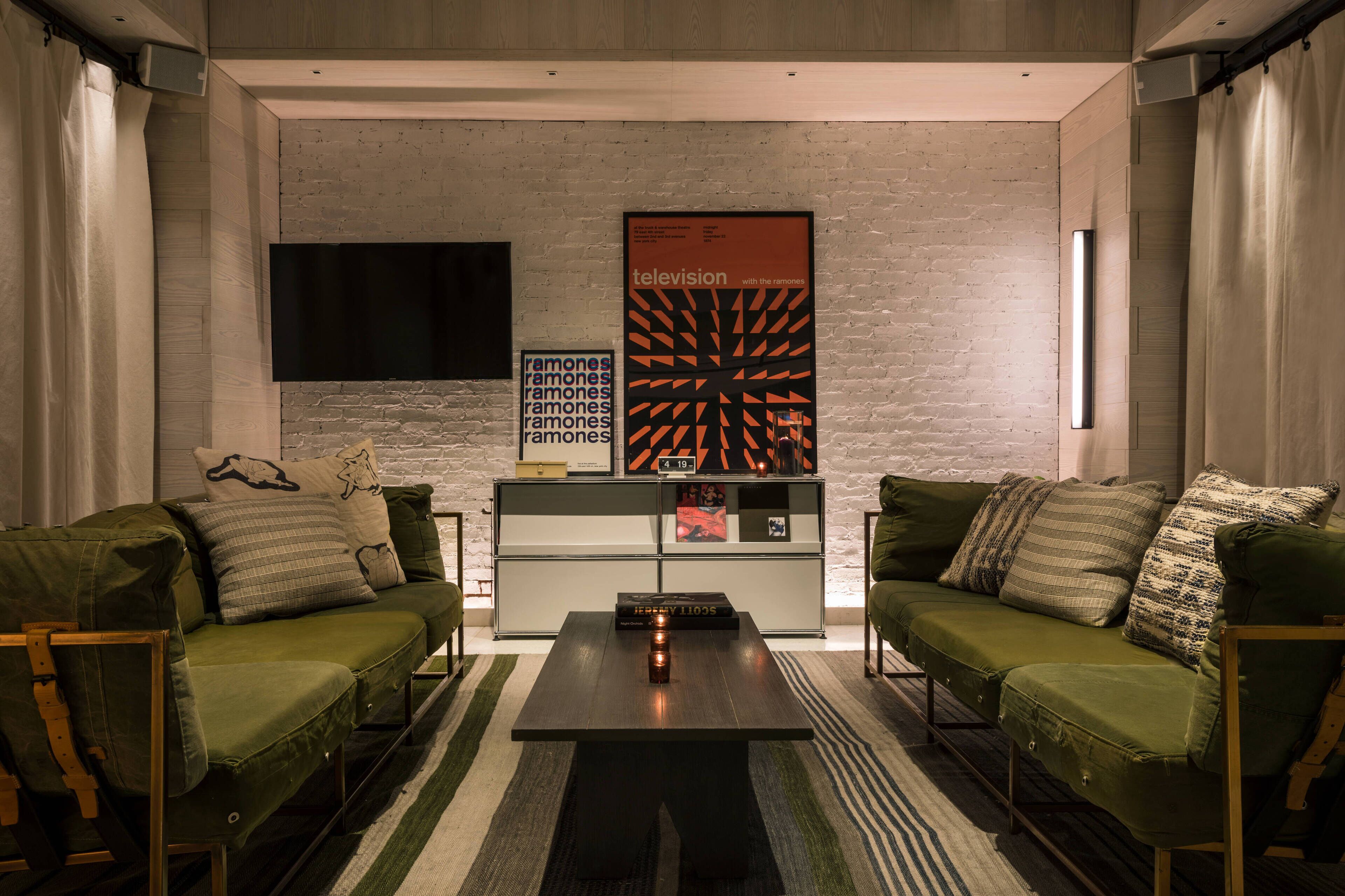 A modern living room with two green sofas, a coffee table, and a flat-screen TV mounted on a brick wall.