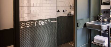 Un baño con baldosas blancas y oscuras, un lavamanos con espejo y un perchero para toallas.