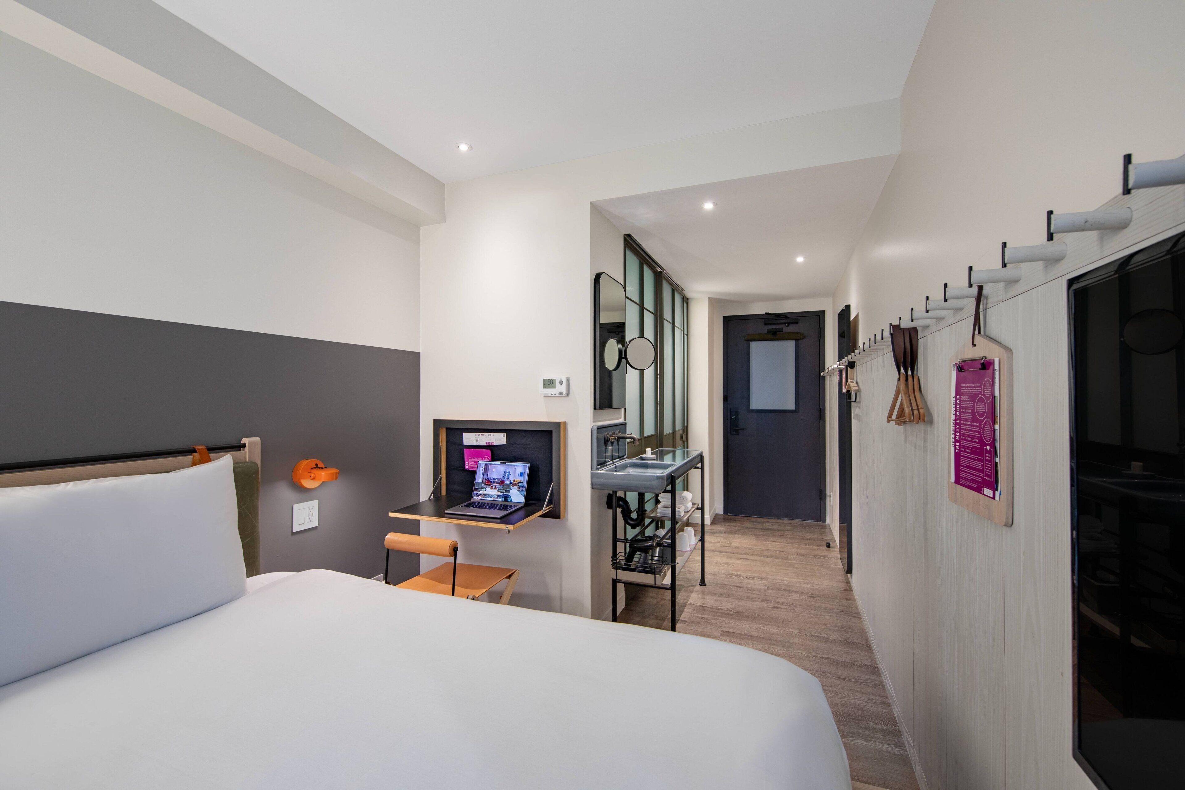 Una habitación de hotel moderna con una cama grande, un escritorio con una computadora portátil, un espejo y una mesita.