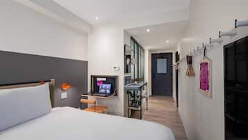 A modern hotel room with a large bed, a desk with a laptop, a mirror, and a small table.