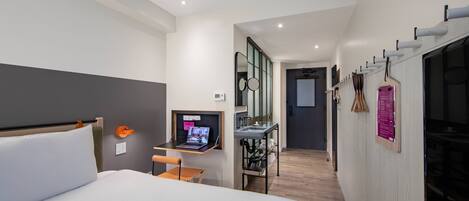 A modern hotel room with a large bed, a desk with a laptop, a mirror, and a small table.