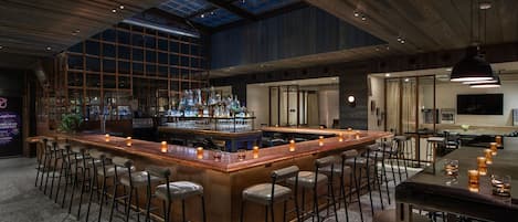 A spacious bar area with a high ceiling and skylight, featuring a long bar counter surrounded by multiple stools.