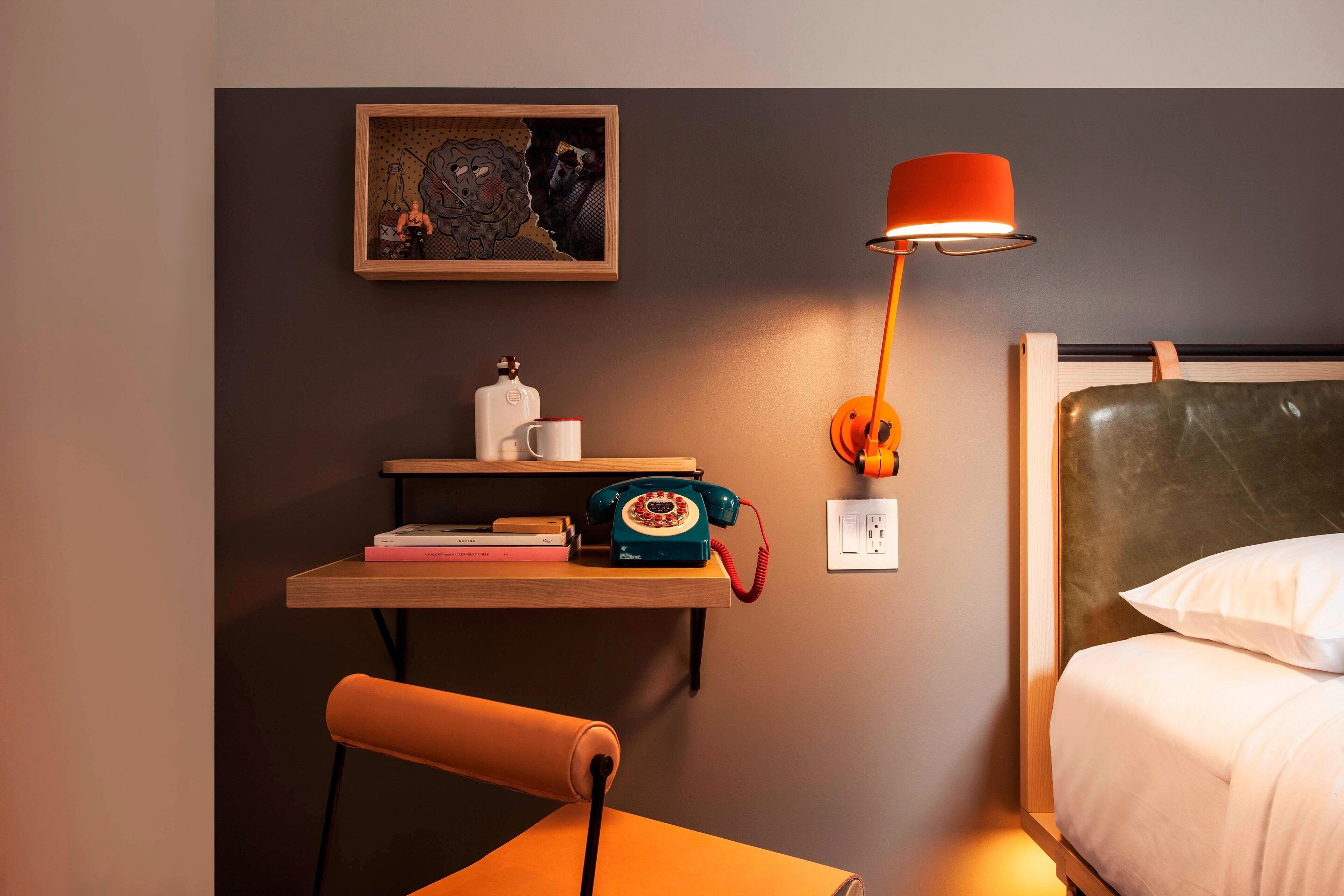Ein Hotelzimmer mit einem Bett, einem Schreibtisch mit Telefon, einem Sessel, einer Lampe und einem Wandbild.