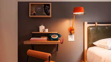 Ein Hotelzimmer mit einem Bett, einem Schreibtisch mit Telefon, einem Sessel, einer Lampe und einem Wandbild.