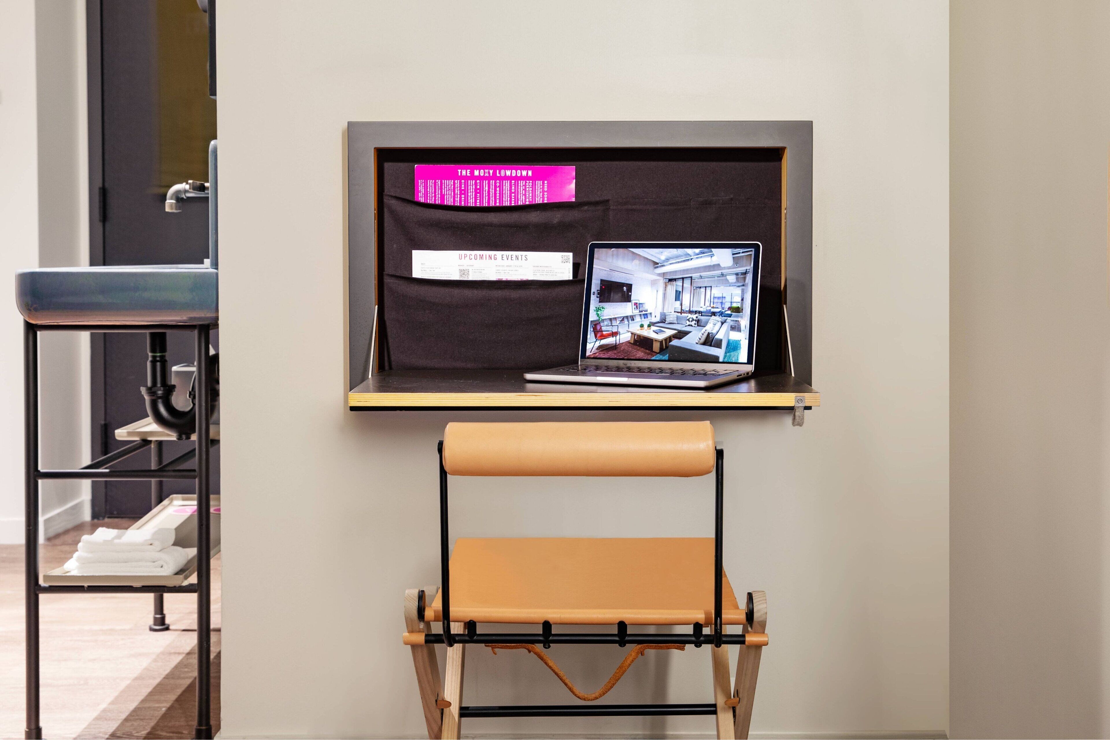A laptop on a shelf with a sign about upcoming events, a foldable chair, and a shelf with towels.