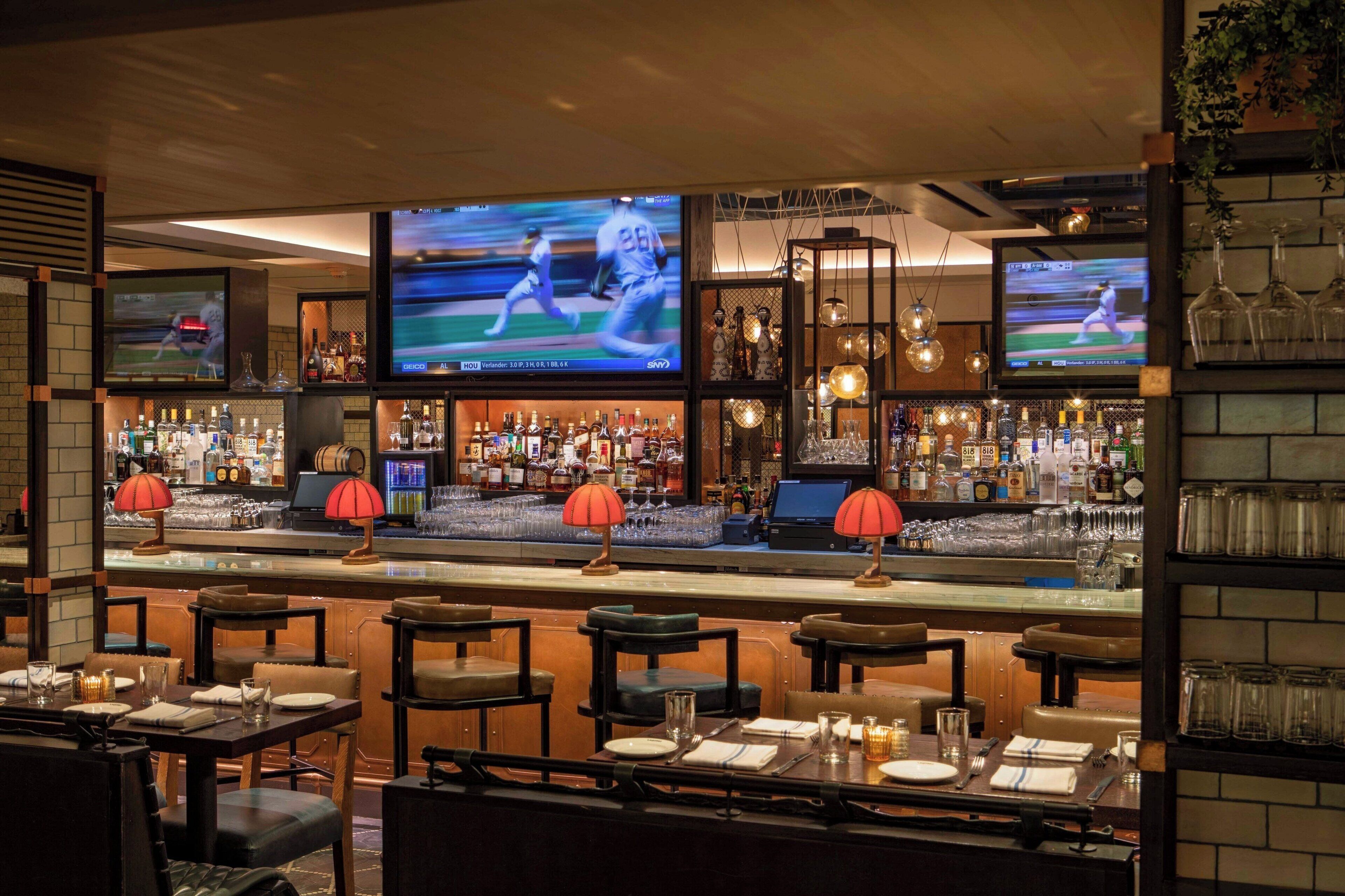 A bar area with multiple TVs displaying sports, a well-stocked bar, and seating with red lamps.