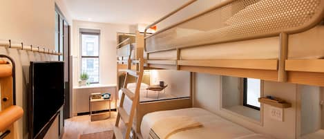 Habitación con literas, televisión, escritorio pequeño, ventana y enchufe.