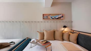 A modern hotel room with a bed, a bedside table with a book and a cup, a wall-mounted artwork, and a headboard with a light fixture.