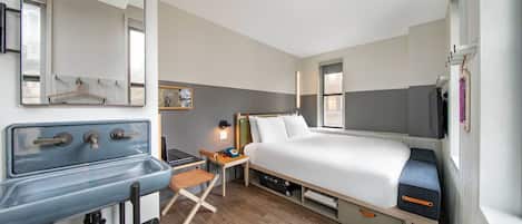Una habitación de hotel pequeña con cama, un escritorio, un espejo y kitchenette.