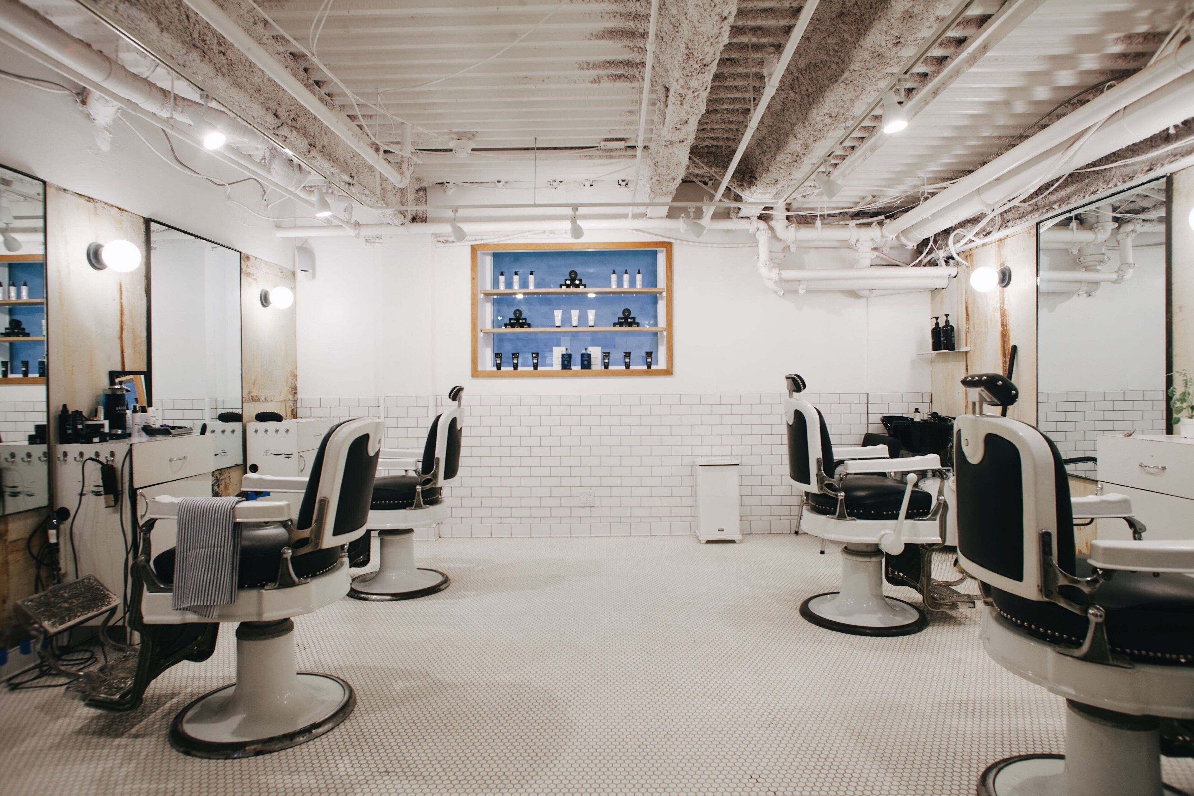 A modern barbershop with three barber chairs, a mirror, and a shelf with grooming products.