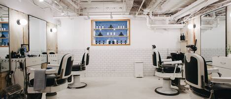 A modern barbershop with three barber chairs, a mirror, and a shelf with grooming products.