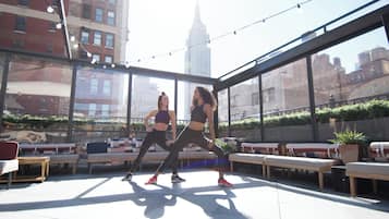 Zona de entrenamiento al aire libre con bancos y equipamiento de ejercicio, con vistas a un paisaje urbano que destaca un edificio.