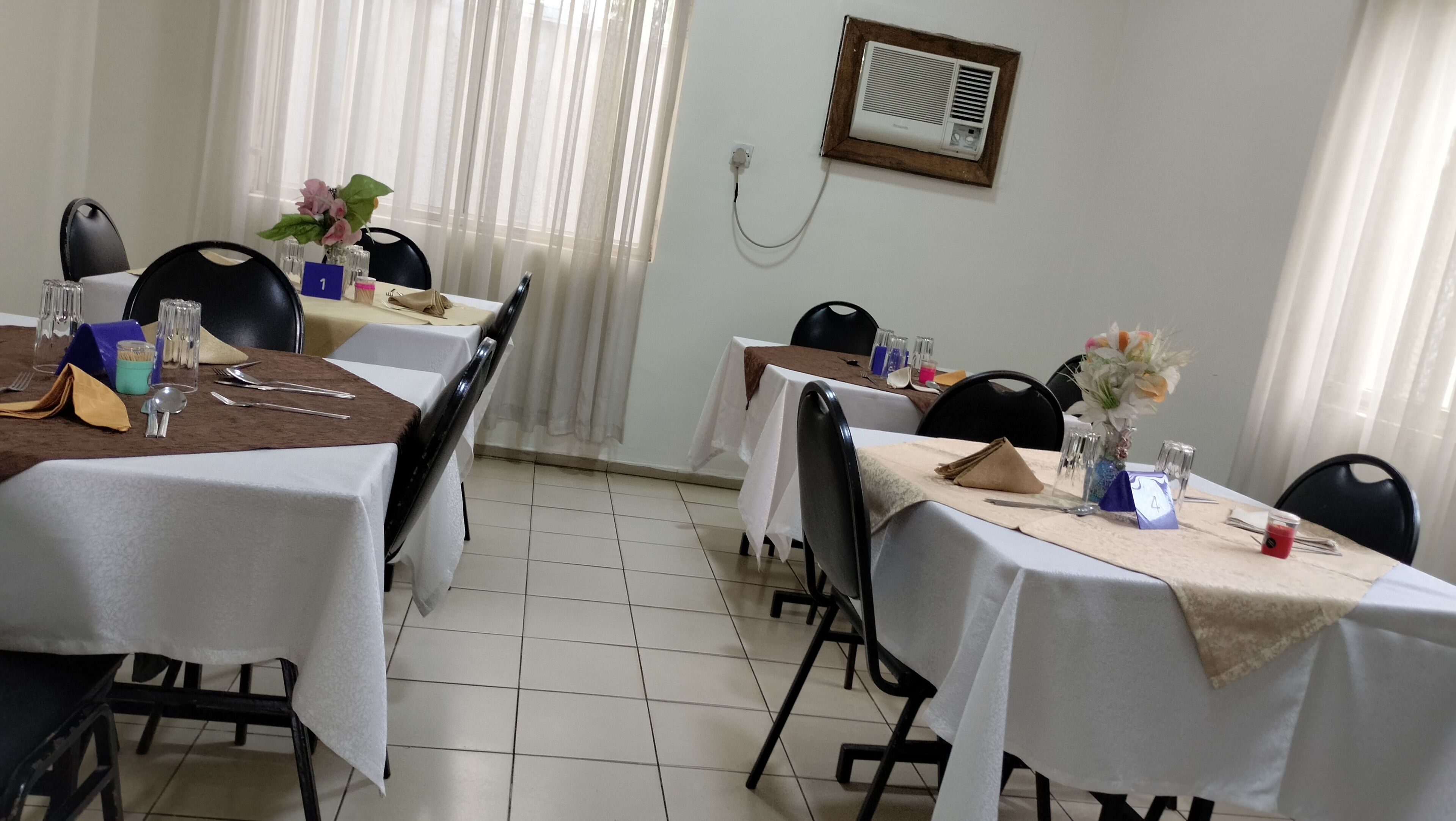Un comedor con mesas dispuestas para cuatro personas, sillas y un aire acondicionado instalado en la pared.