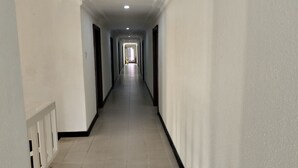 En lång, smal hall med vita väggar och ett kaklat golv, som leder till ett ljust rum längst in.