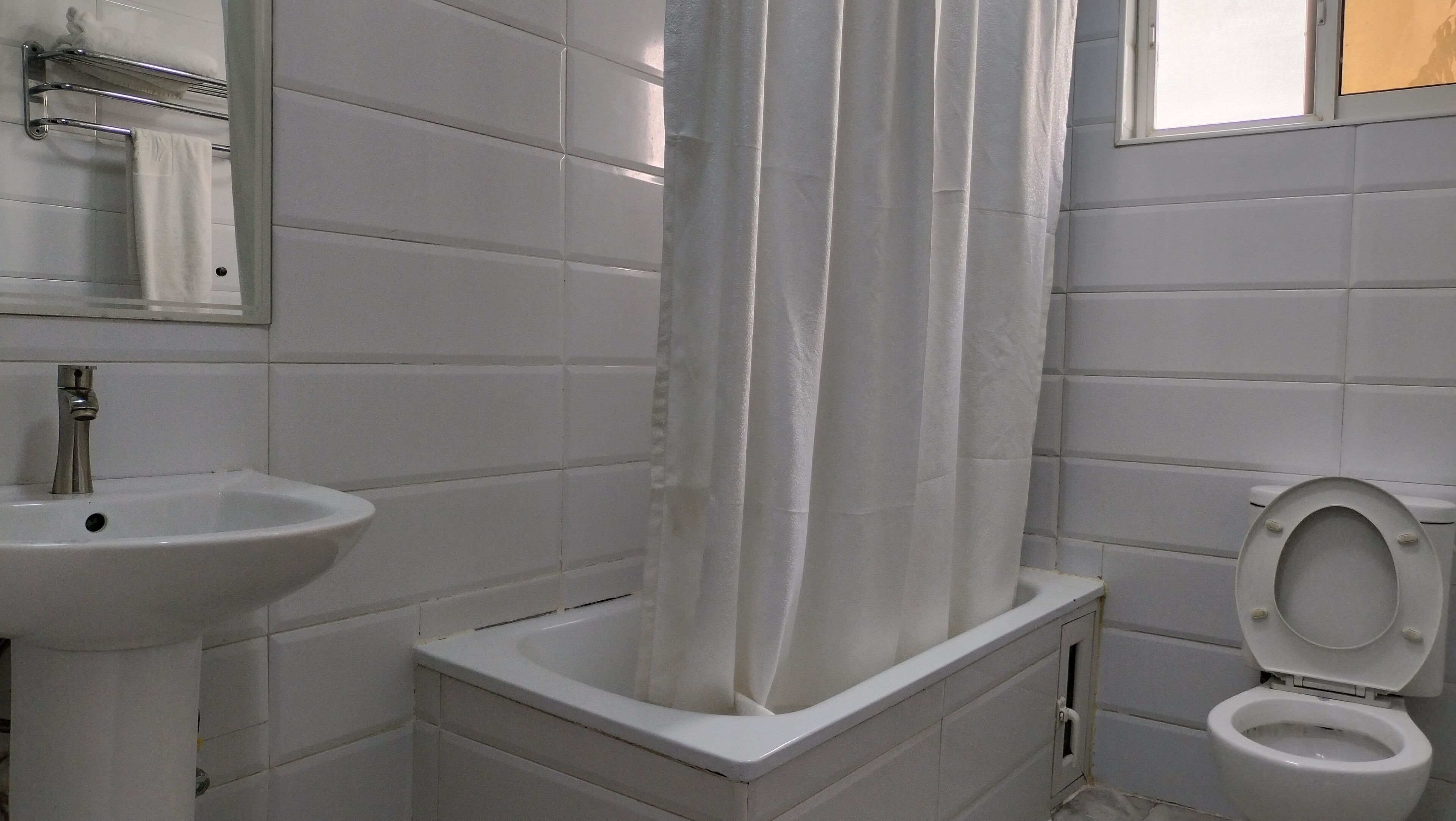Un bagno con piastrelle bianche, un lavandino, un water e una tenda della doccia.