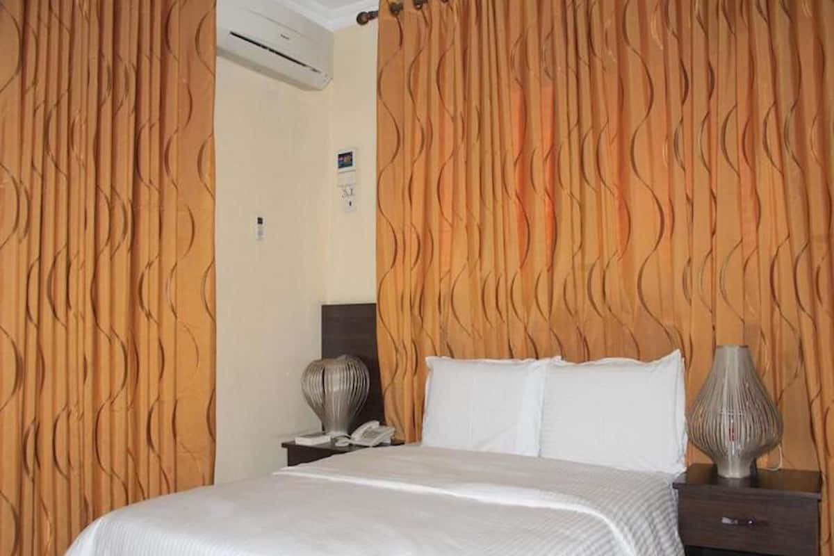 A hotel room with a bed, a nightstand, a lamp, and a wall-mounted air conditioner.