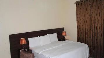 Habitación de hotel con una cama grande, dos lámparas de noche, un cabecero de madera y una cortina de estampado ondulado.