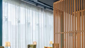 A modern lobby with a seating area, a wooden partition, and a large window with sheer curtains.