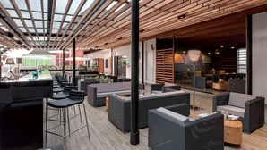 Un espace extérieur moderne, aménagé pour se détendre, avec de hauts plafonds et un toit en verre, comprenant des meubles en osier et une table centrale.