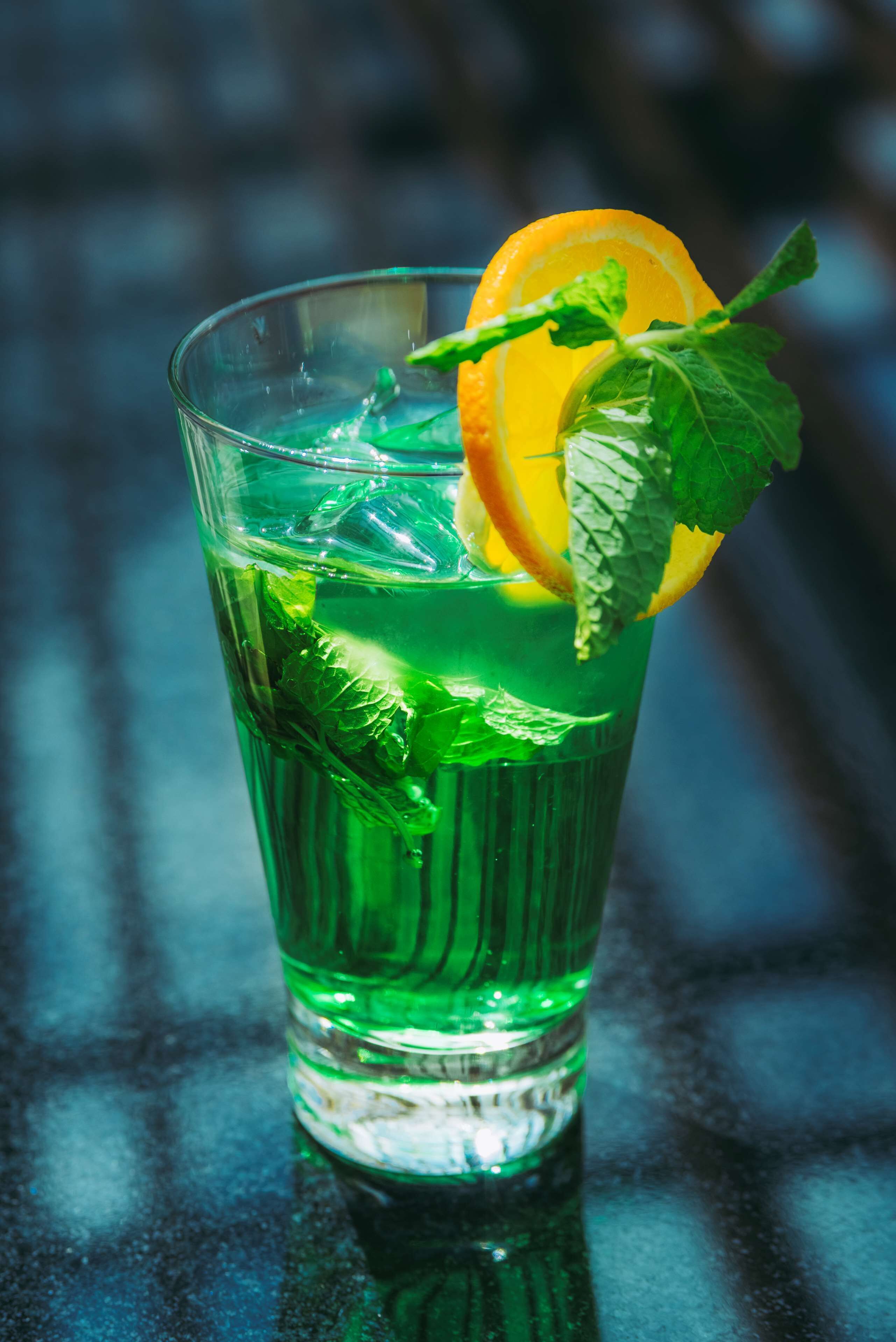 A glass of green beverage with ice, garnished with mint leaves and an orange slice.