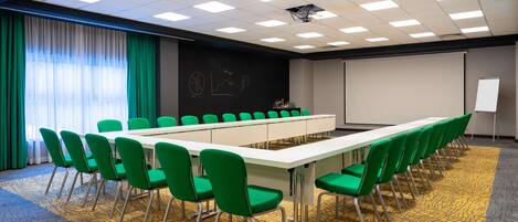 A conference room with a long table, green chairs, a projector screen, and a whiteboard.