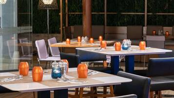 A restaurant with tables set for dining, chairs, and a large potted plant in the background.