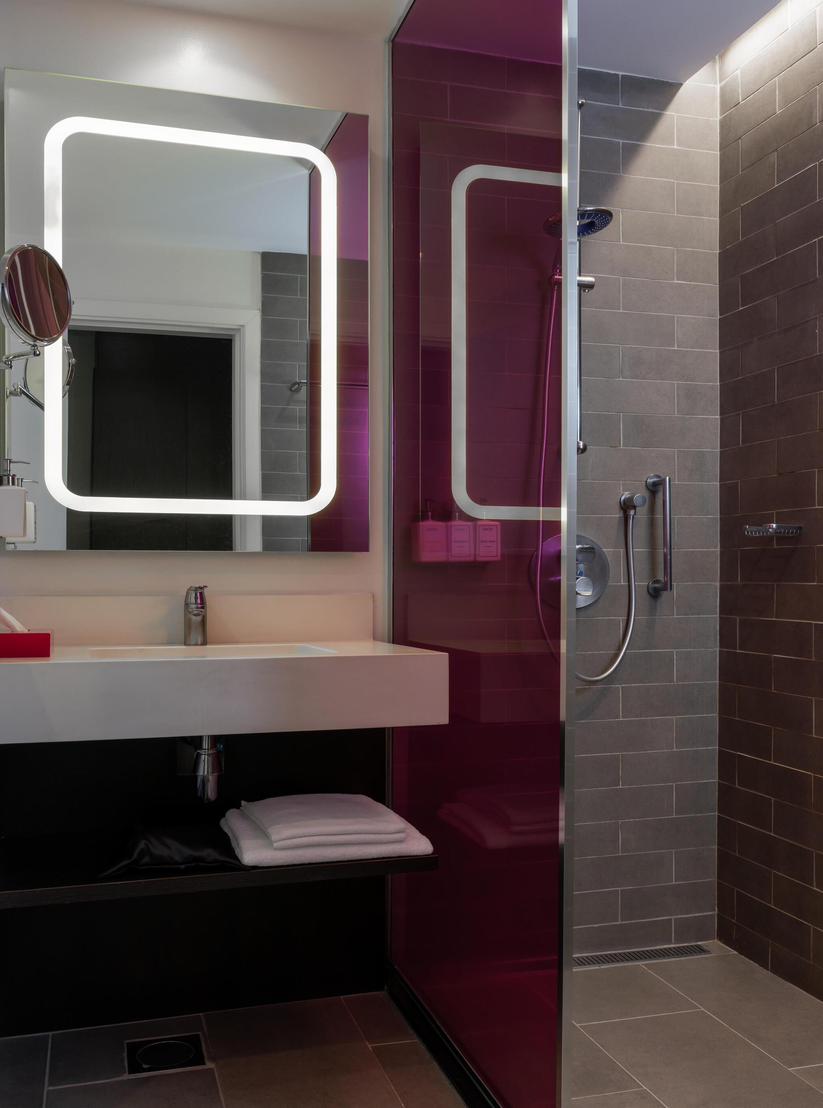 A modern bathroom with a vanity, a mirror with illuminated frame, a shower with a glass door, and a towel rack.