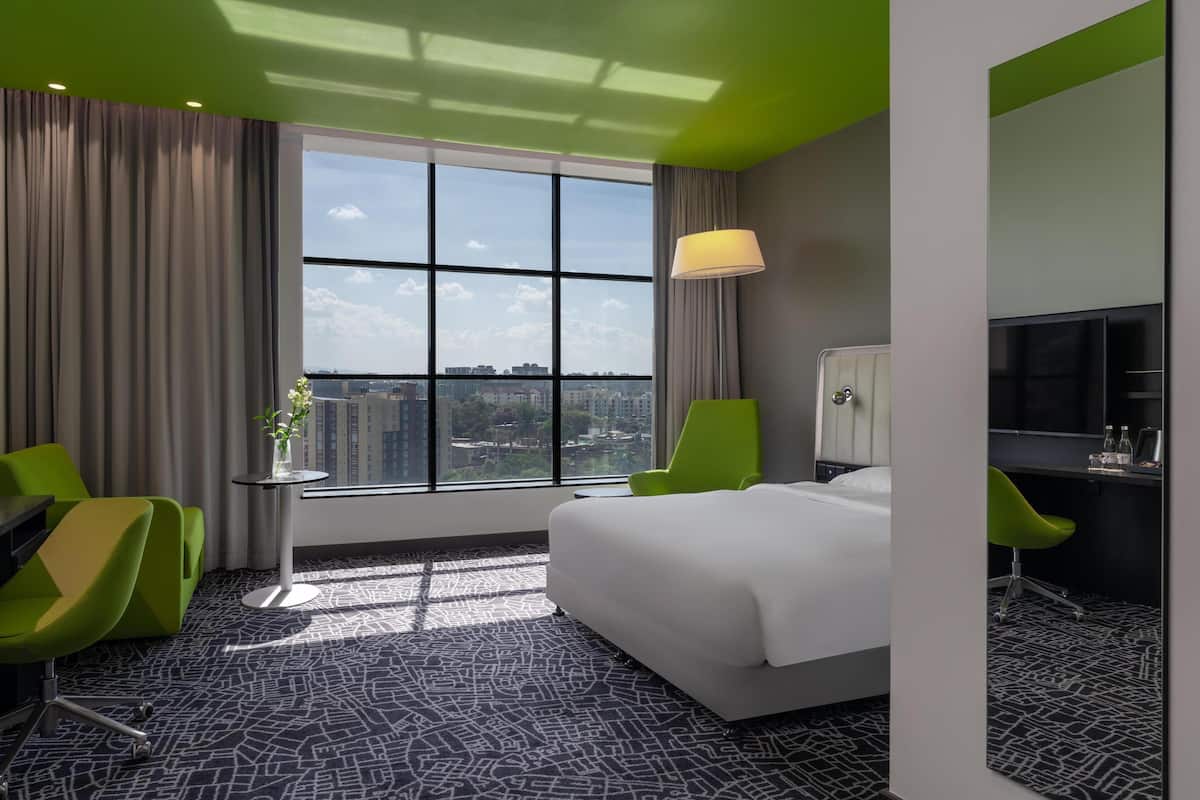 Une chambre d’hôtel avec une grande fenêtre, un lit, un bureau, une chaise et un téléviseur.