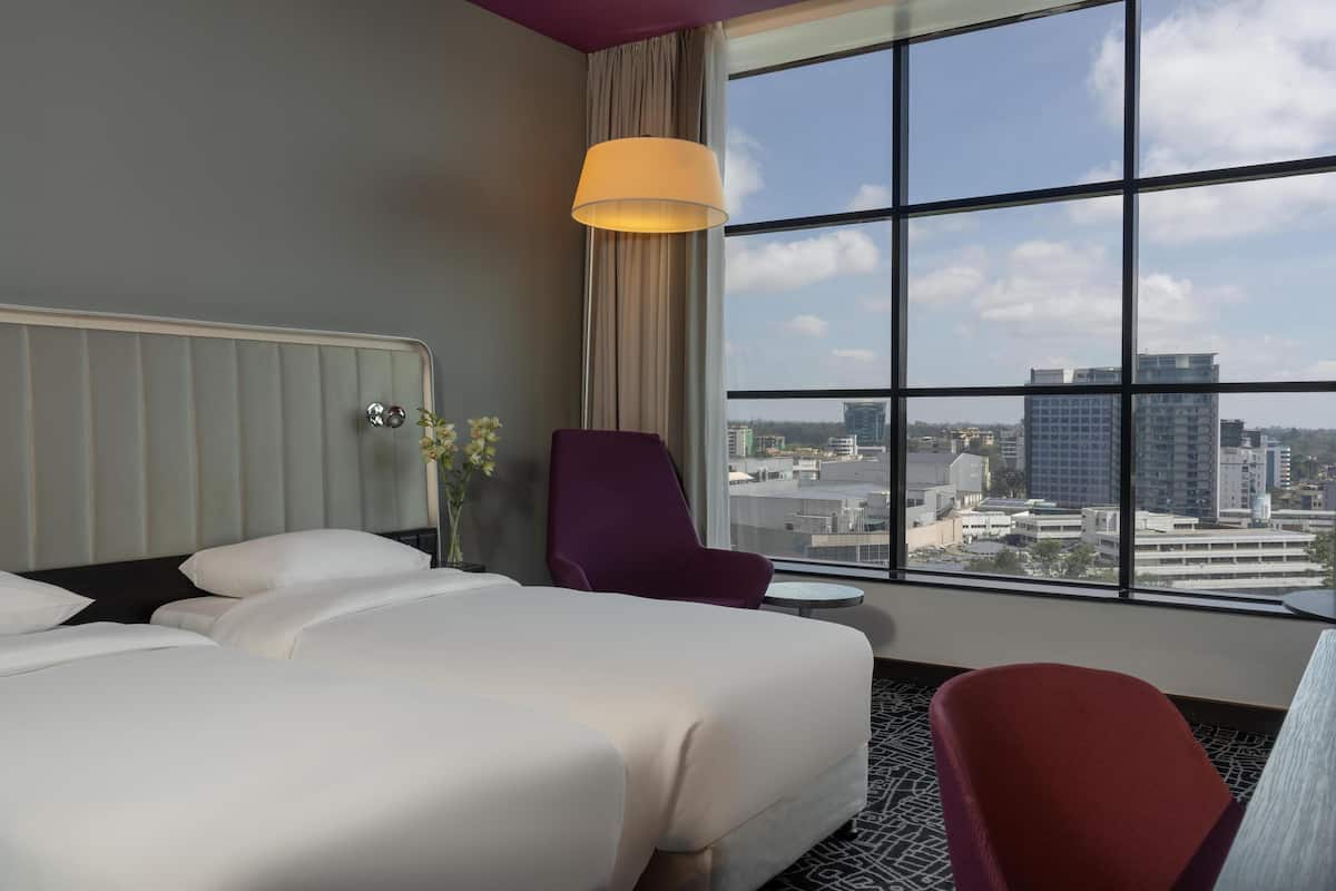 Une chambre d’hôtel avec une grande fenêtre, un lit, une chaise et une petite table.