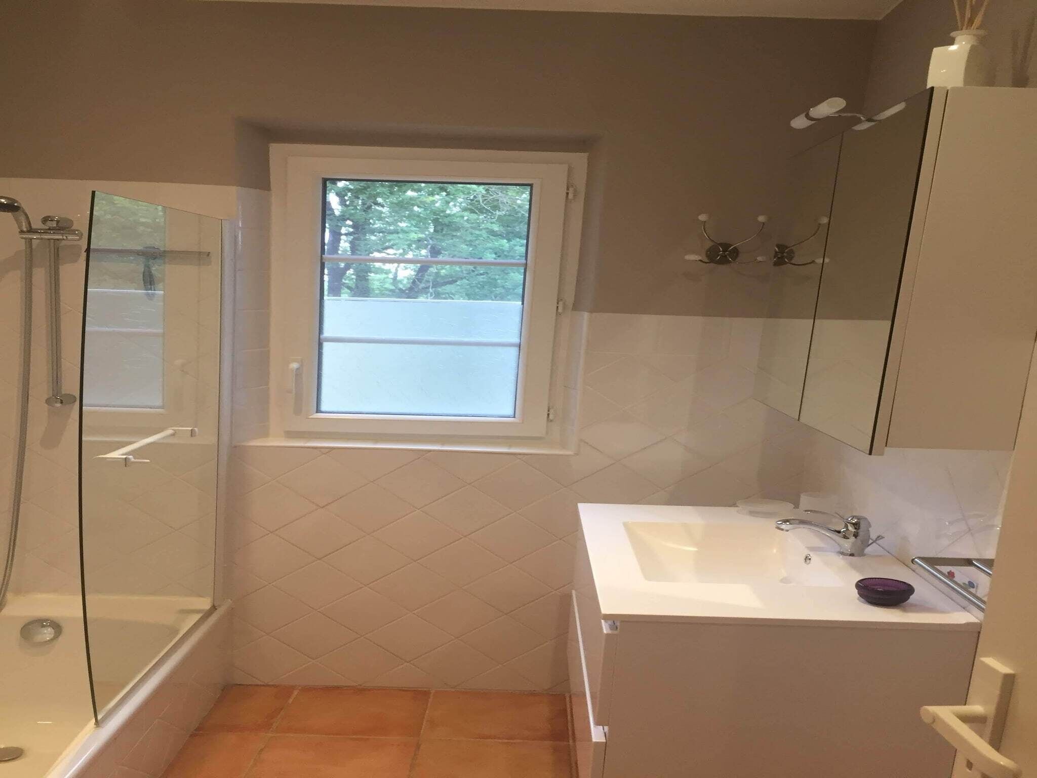 A bathroom with a glass-enclosed shower, a window, a sink, and a mirror.